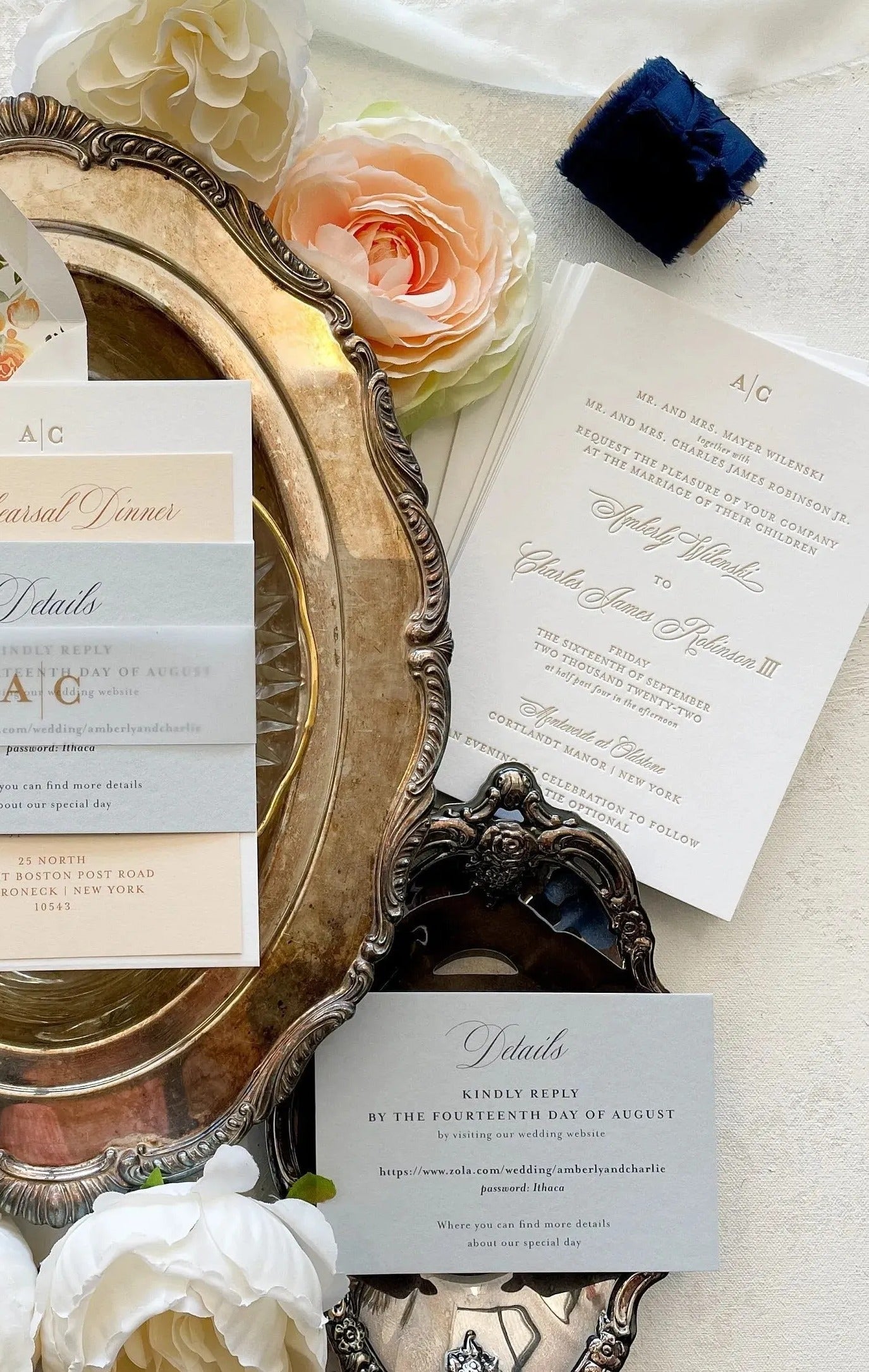 a wedding invitation with floral designs, a silver tray, and various other wedding-related items such as a blue ribbon, a white card, and a white rose.