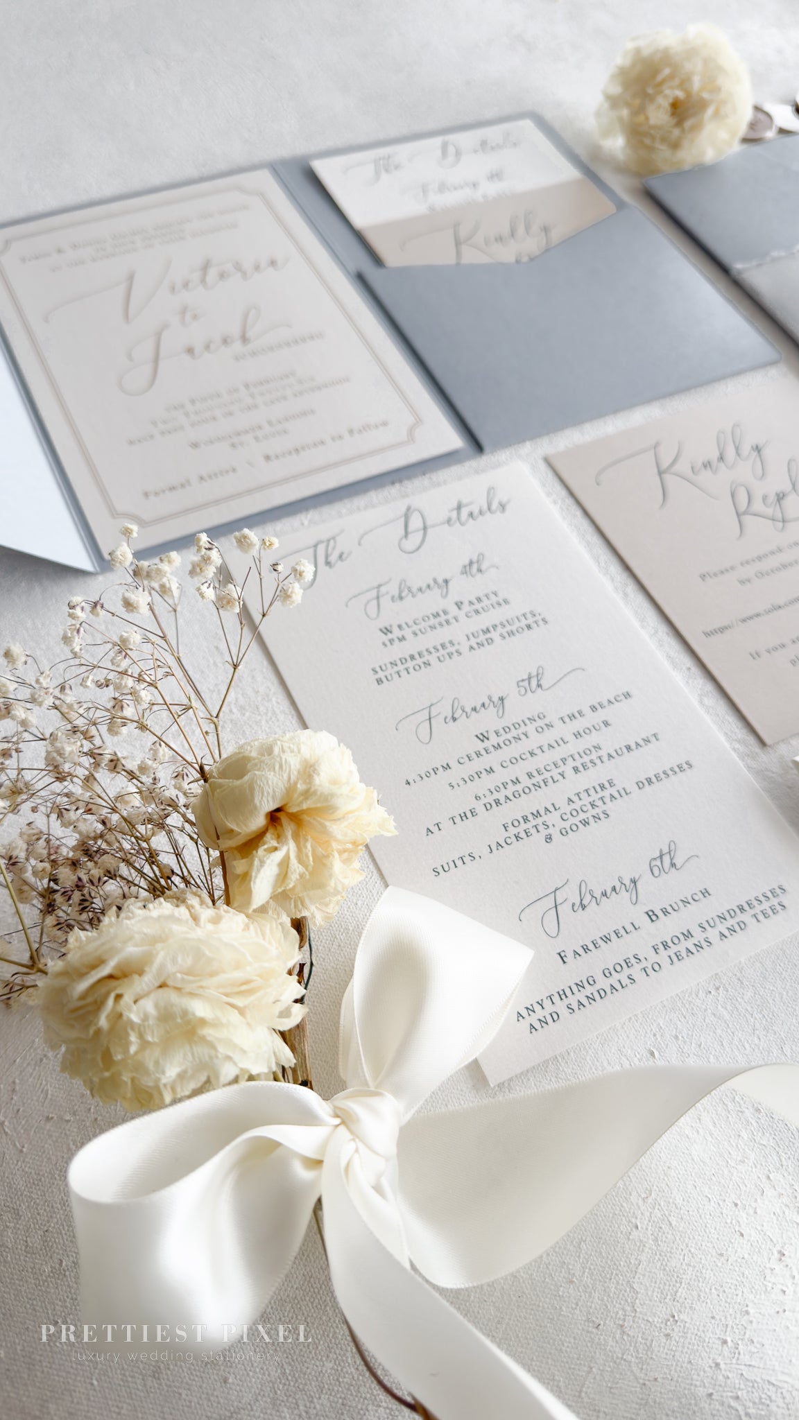 a wedding invitation suite with a white ribbon, delicate white flowers, and a small white flower arrangement.