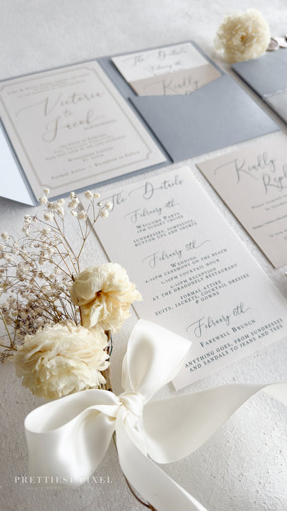 a wedding invitation suite with a white ribbon, delicate white flowers, and a small white flower arrangement.
