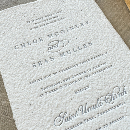 White textured wedding invitation with black text on a gray surface