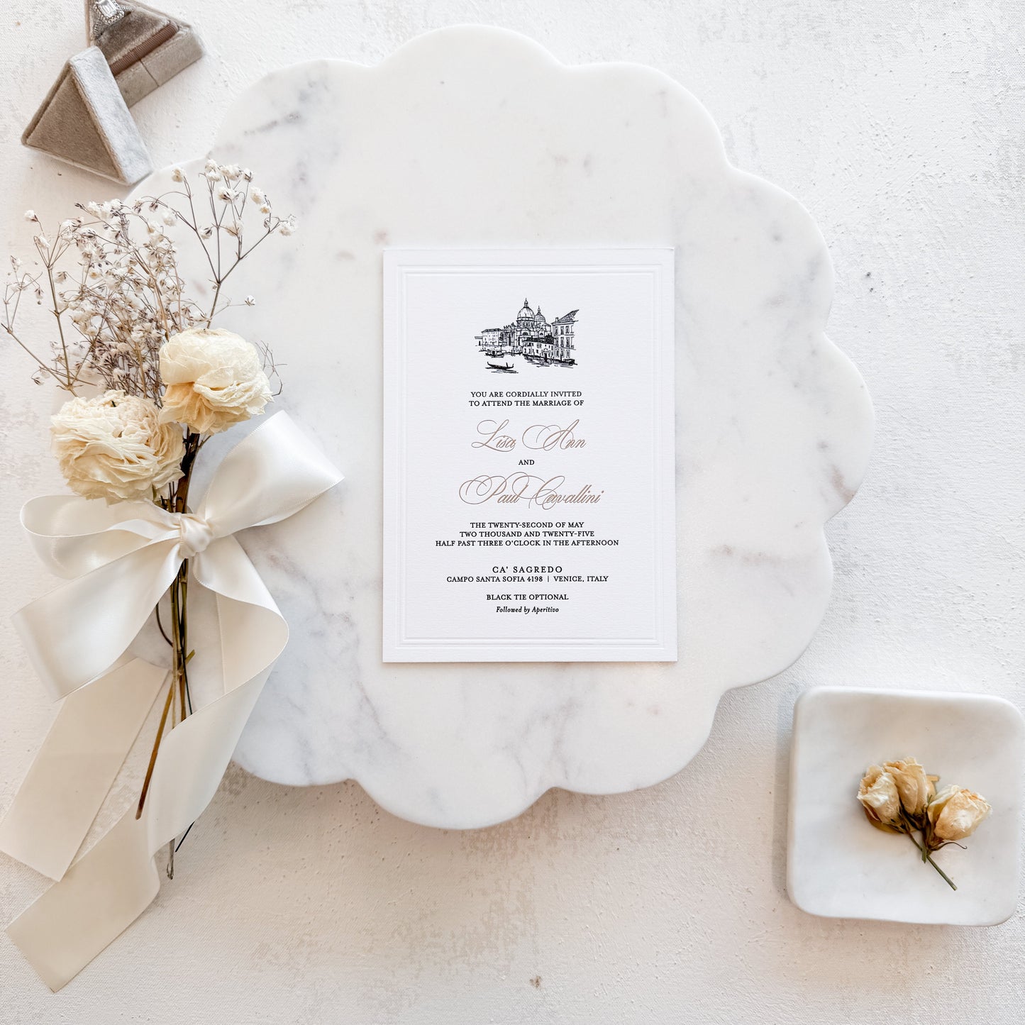 Wedding invitation card on a marble surface with flowers and a decorative box.