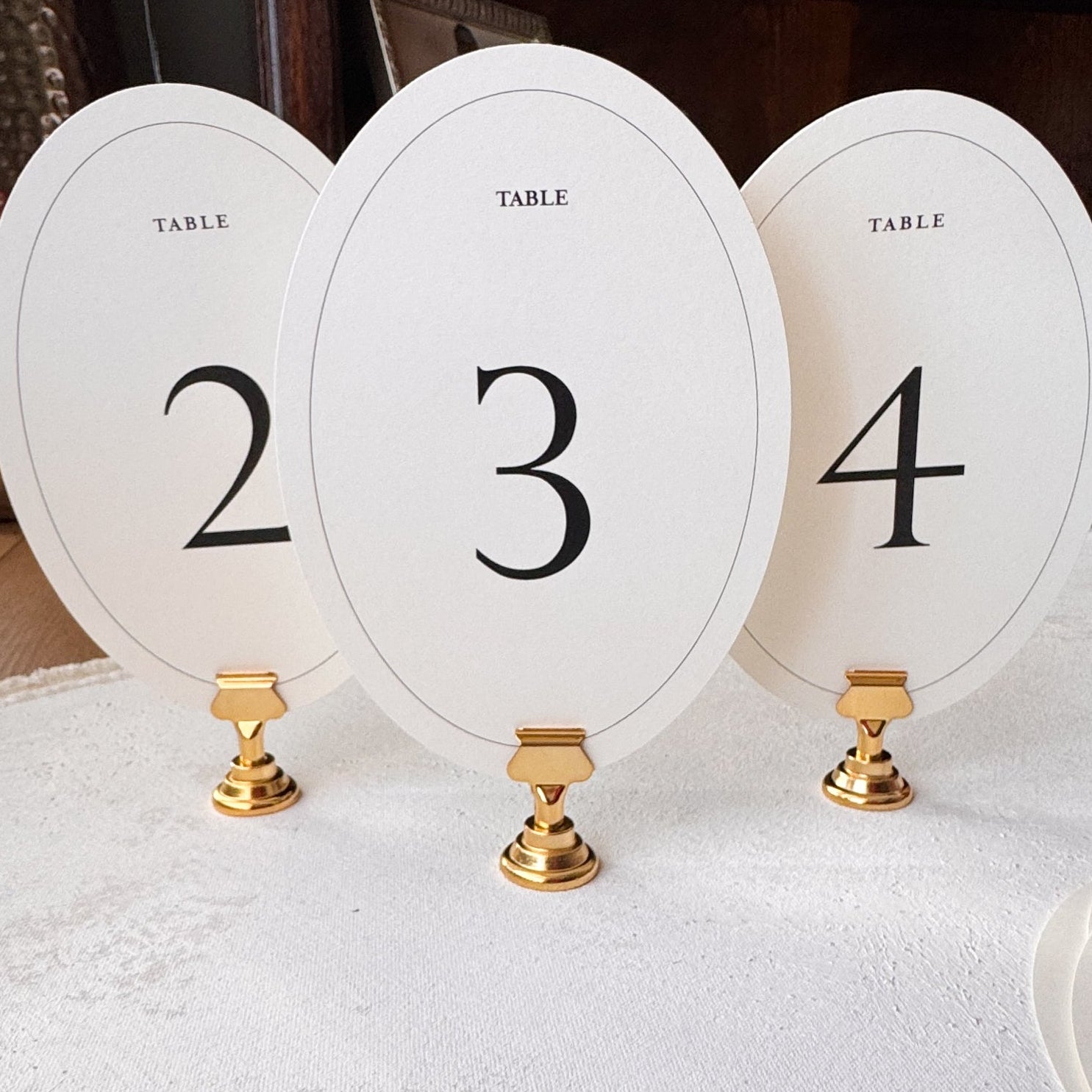Three oval table number holders with numbers 2, 3, and 4 on a white surface.