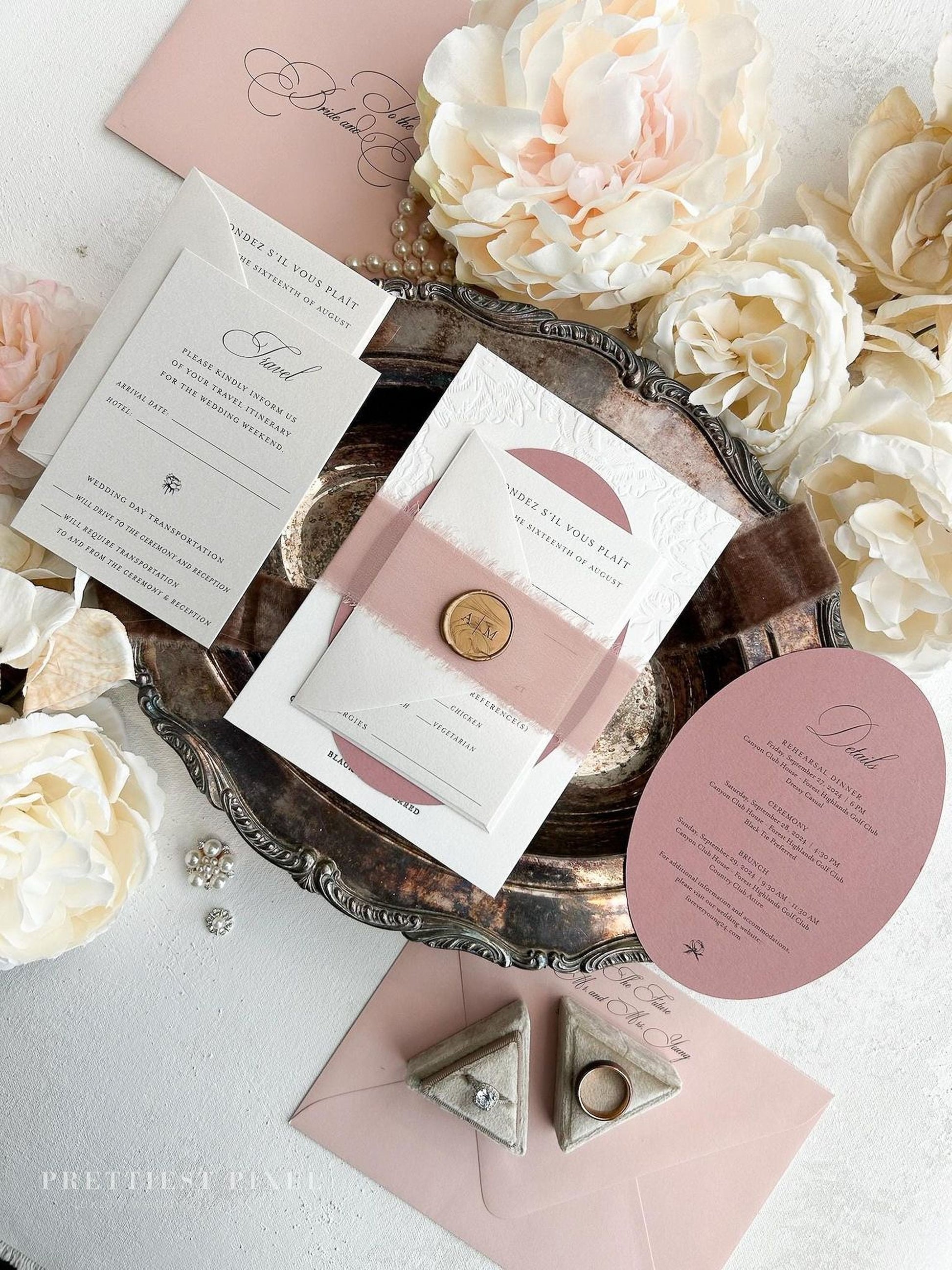 a wedding invitation with a pink and white color scheme, surrounded by various wedding-related items such as flowers, jewelry, and a metal tray.