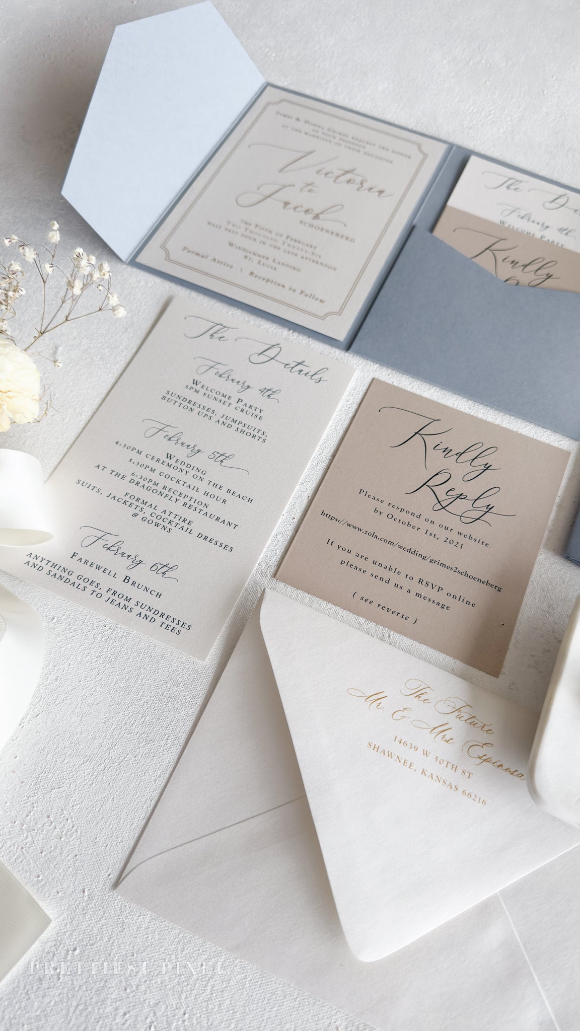 A wedding invitation featuring a light blue background with gold cursive text, accompanied by a white envelope and a small bouquet of white flowers.