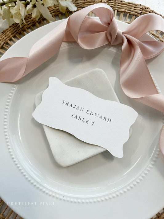 a place setting with a place card and a pink ribbon